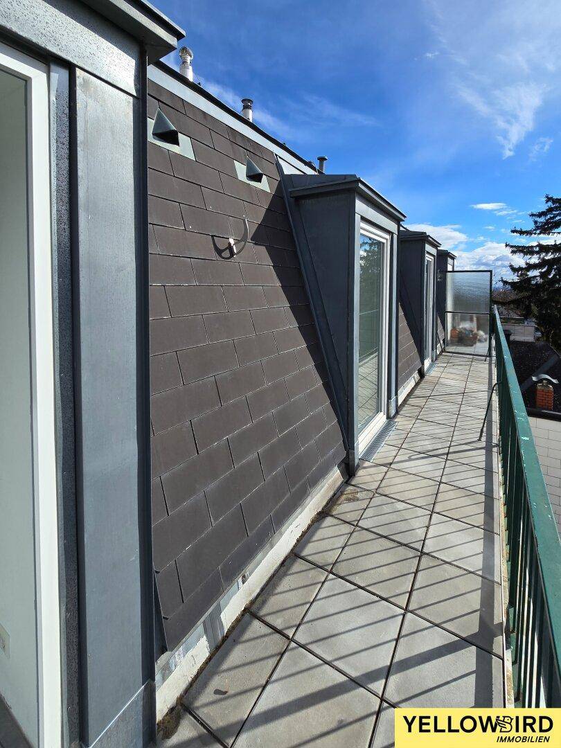 Langer, gefliester Balkon mit Blick auf die Umgebung und blauen Himmel.