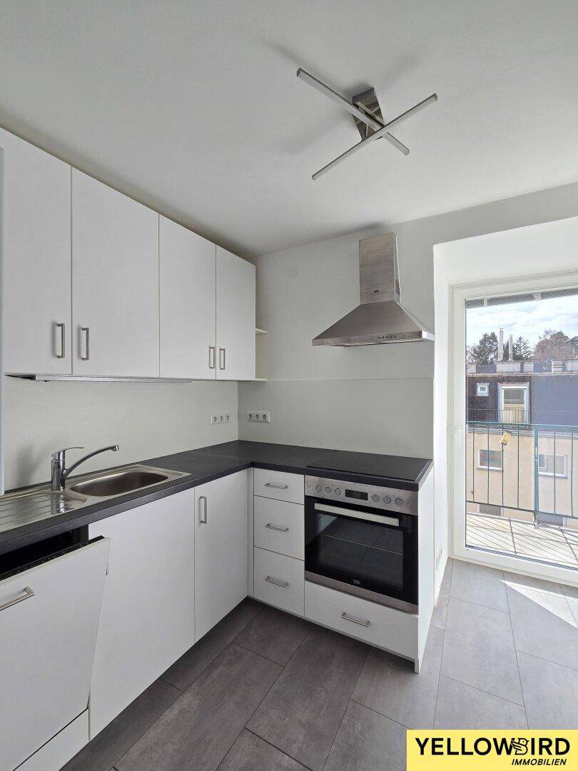 Moderne Einbauküche mit weißen Schränken, dunkler Arbeitsplatte und Zugang zum Balkon.