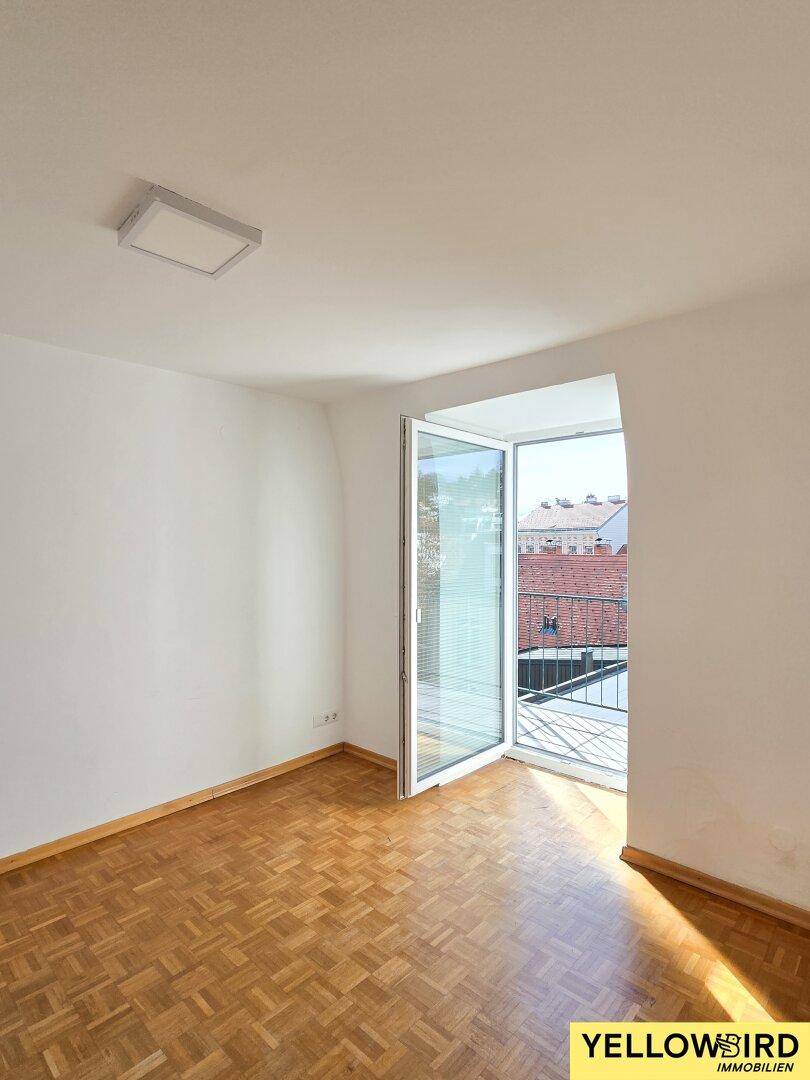 Helles Zimmer mit Parkettboden und Zugang zu einem kleinen Balkon.
