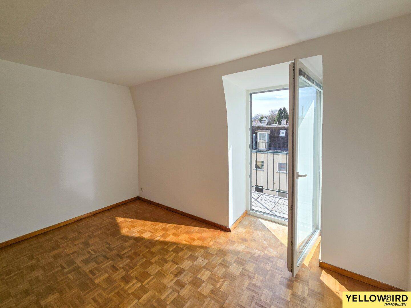 Helles Zimmer im Dachgeschoss mit Parkettboden und Zugang zum Balkon.