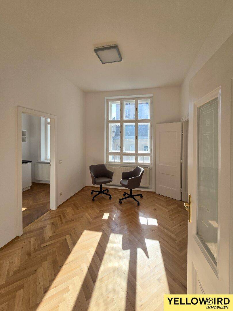 Helles Zimmer mit Fischgrätparkett und großem Fenster, das viel Sonnenlicht empfängt.