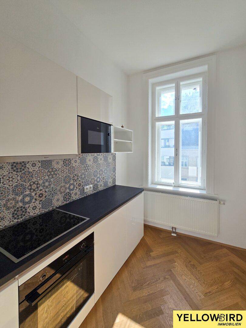 Moderne Küche mit weißen Schränken, Induktionskochfeld und gemustertem Fliesenspiegel.