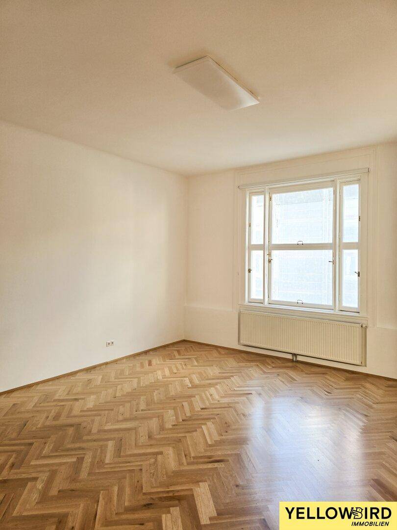 Leeres Zimmer mit Fischgrätparkett und großem Fenster, bereit zur individuellen Gestaltung.