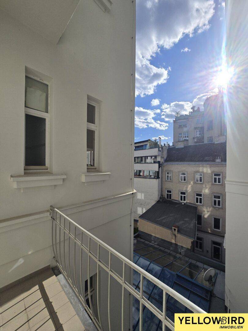 Kleiner Balkon mit Blick auf die umliegenden Gebäude und den sonnigen Himmel.