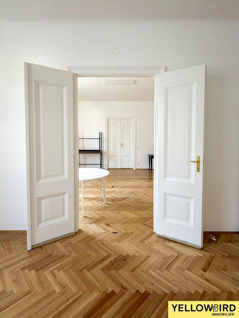 Blick durch geöffnete Flügeltüren in ein weiteres Zimmer mit Fischgrätparkett.