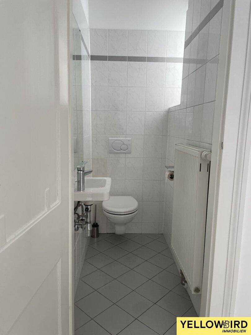 Kleines Gäste-WC mit Waschbecken, Toilette und grauen Bodenfliesen.