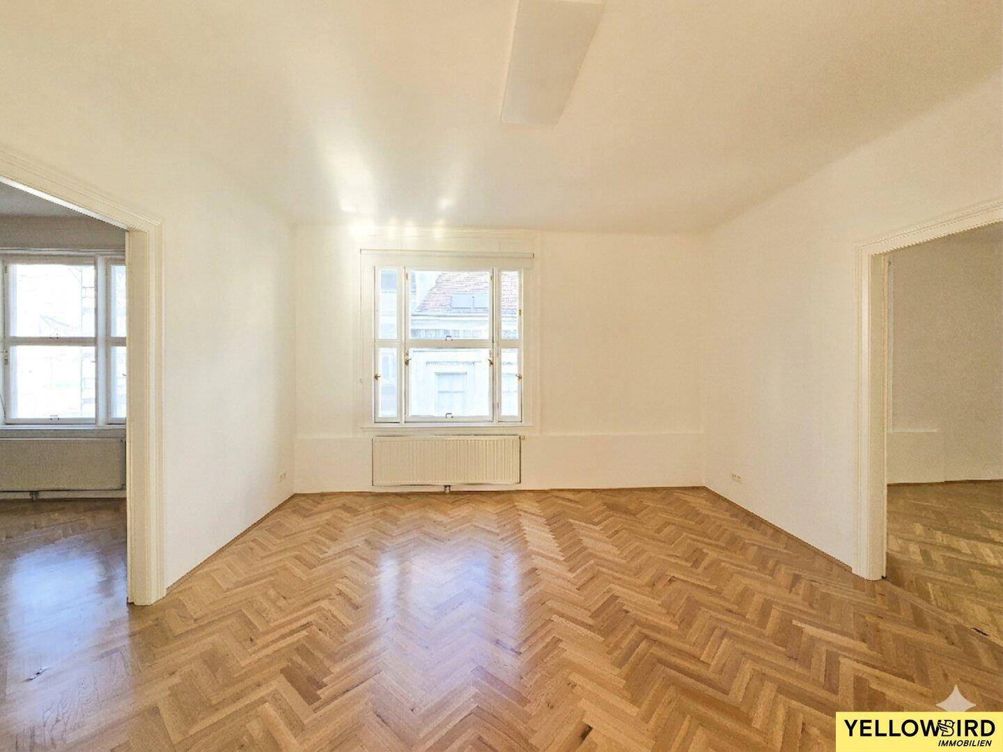 Geräumiges Zimmer mit Fischgrätparkett und Fenster, das viel Tageslicht hereinlässt.