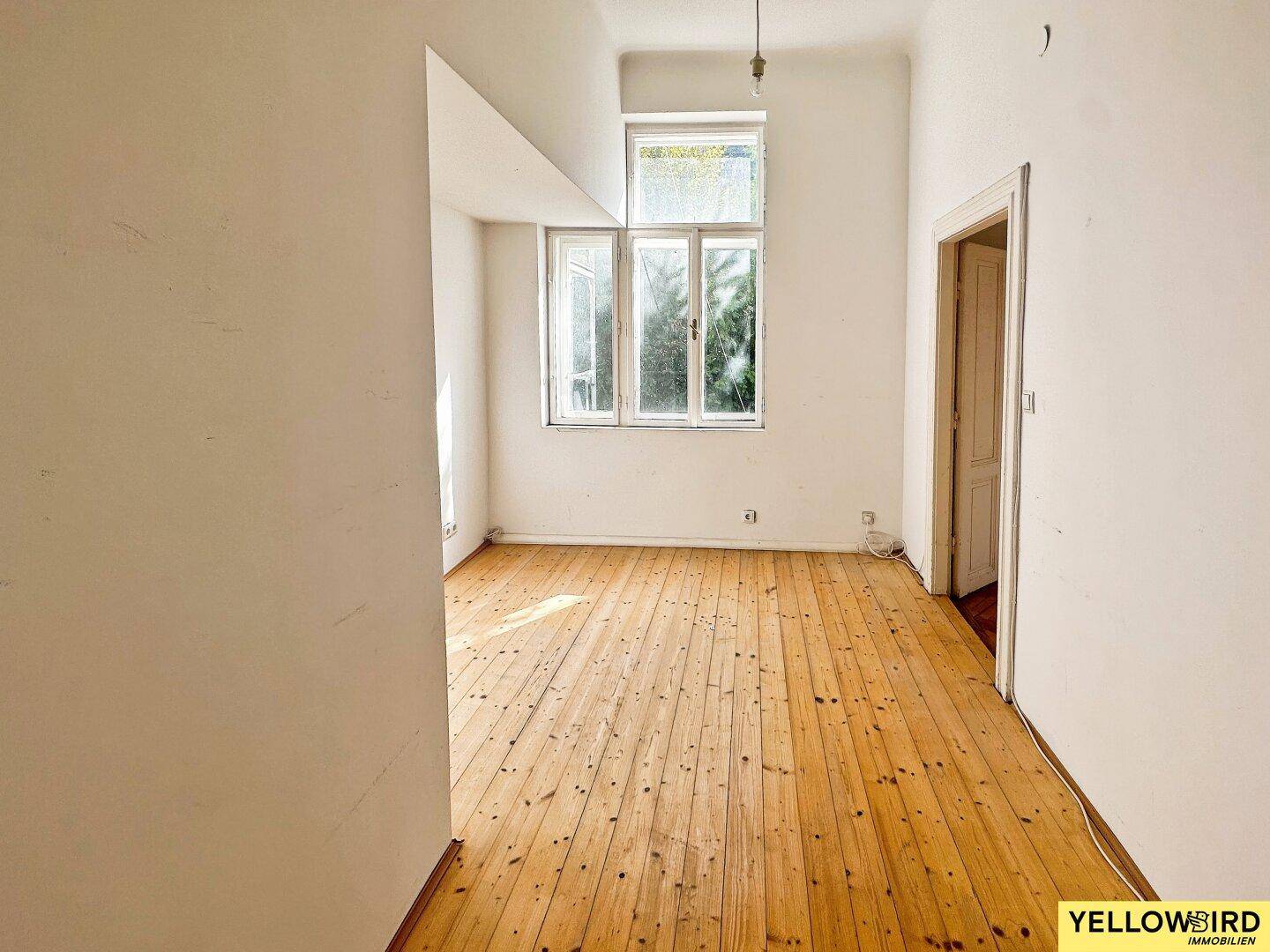 Leerer Raum mit Dielenboden und großen Fenstern, bereit für eine Modernisierung.