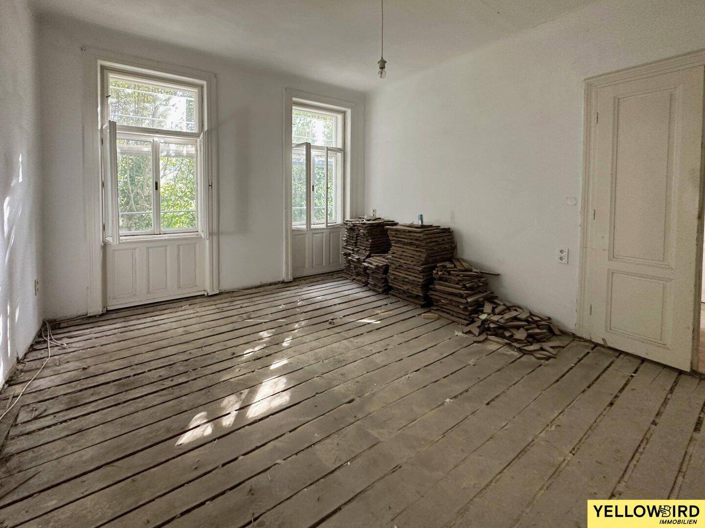 Renovierungsbedürftiger Raum mit freigelegtem Dielenboden und Resten des alten Parketts.