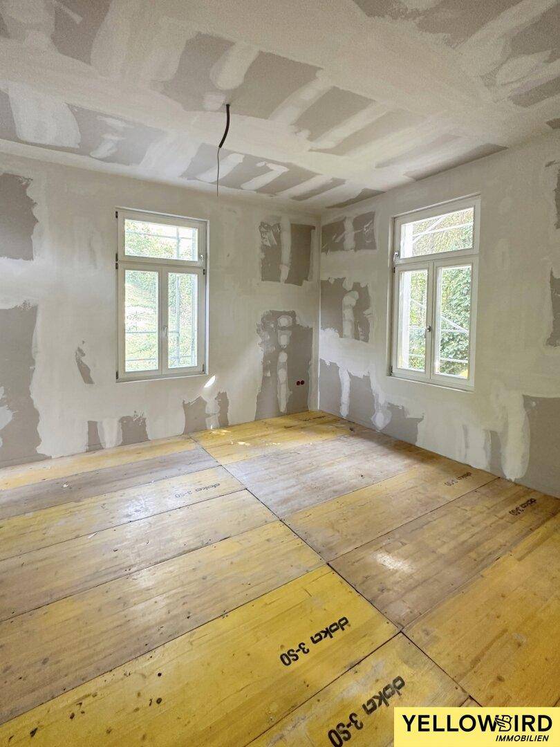 Raum im Rohbauzustand mit gespachtelten Wänden und vorbereitetem Boden für den Ausbau.