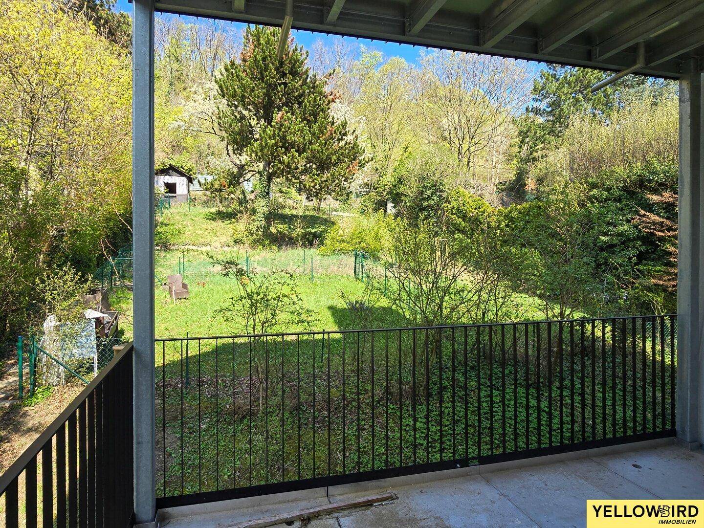 Balkon mit Blick auf einen üppigen grünen Garten und bewaldete Hügel.