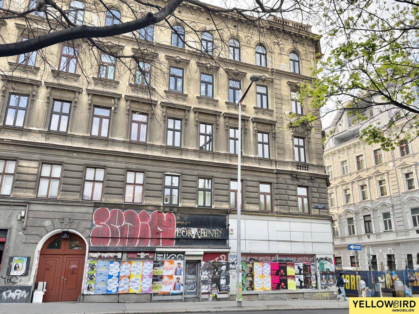 Historische Gebäudefassade mit vielen Fenstern, Graffiti und Plakaten im Erdgeschossbereich.
