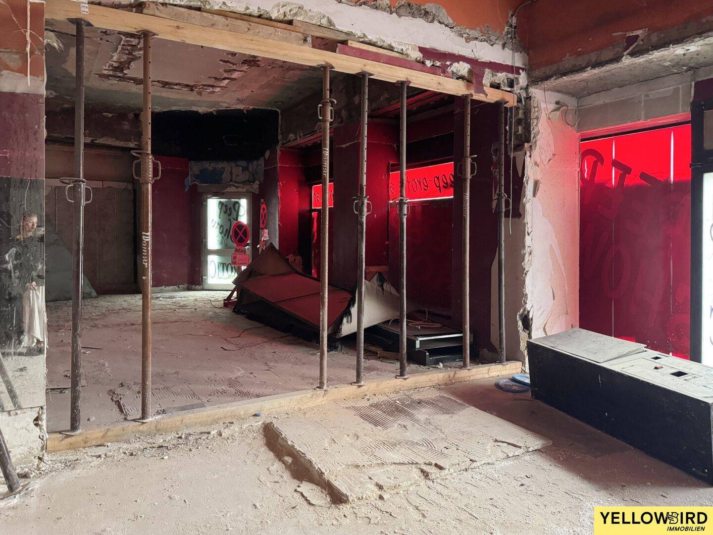 Innenraum im Rohbauzustand mit temporären Stützen und roten Wänden, bereit für die Renovierung.