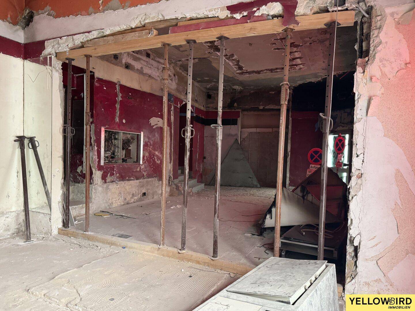 Blick in einen weiteren Bereich des Innenraums im Rohbau mit Stützpfeilern und roten Wänden.