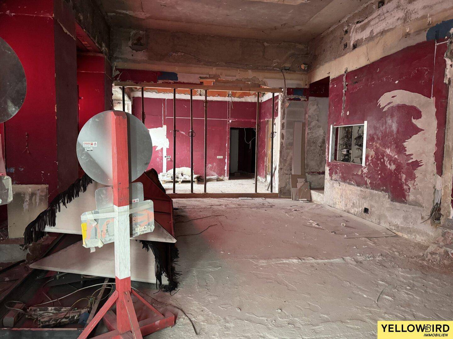 Weitläufiger Innenraum im Rohbau mit roten Wänden, Betonboden und sichtbaren Renovierungsarbeiten.