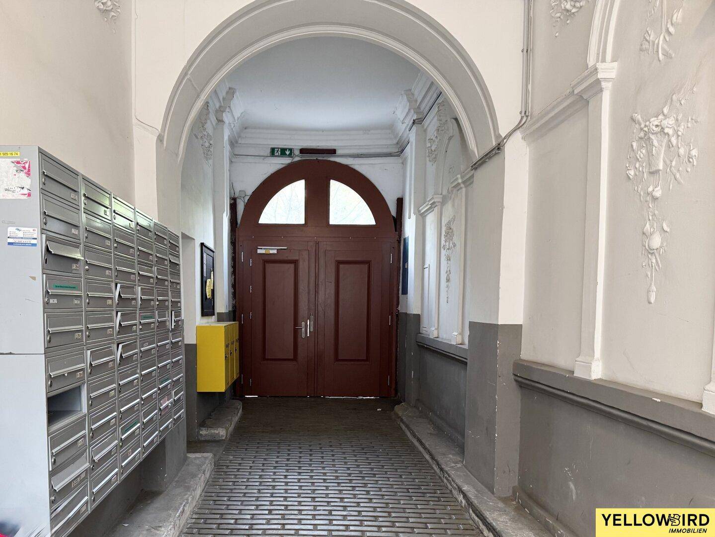 Eingangsbereich eines Altbaus mit Briefkästen, einem großen Holztor und Stuckverzierungen.