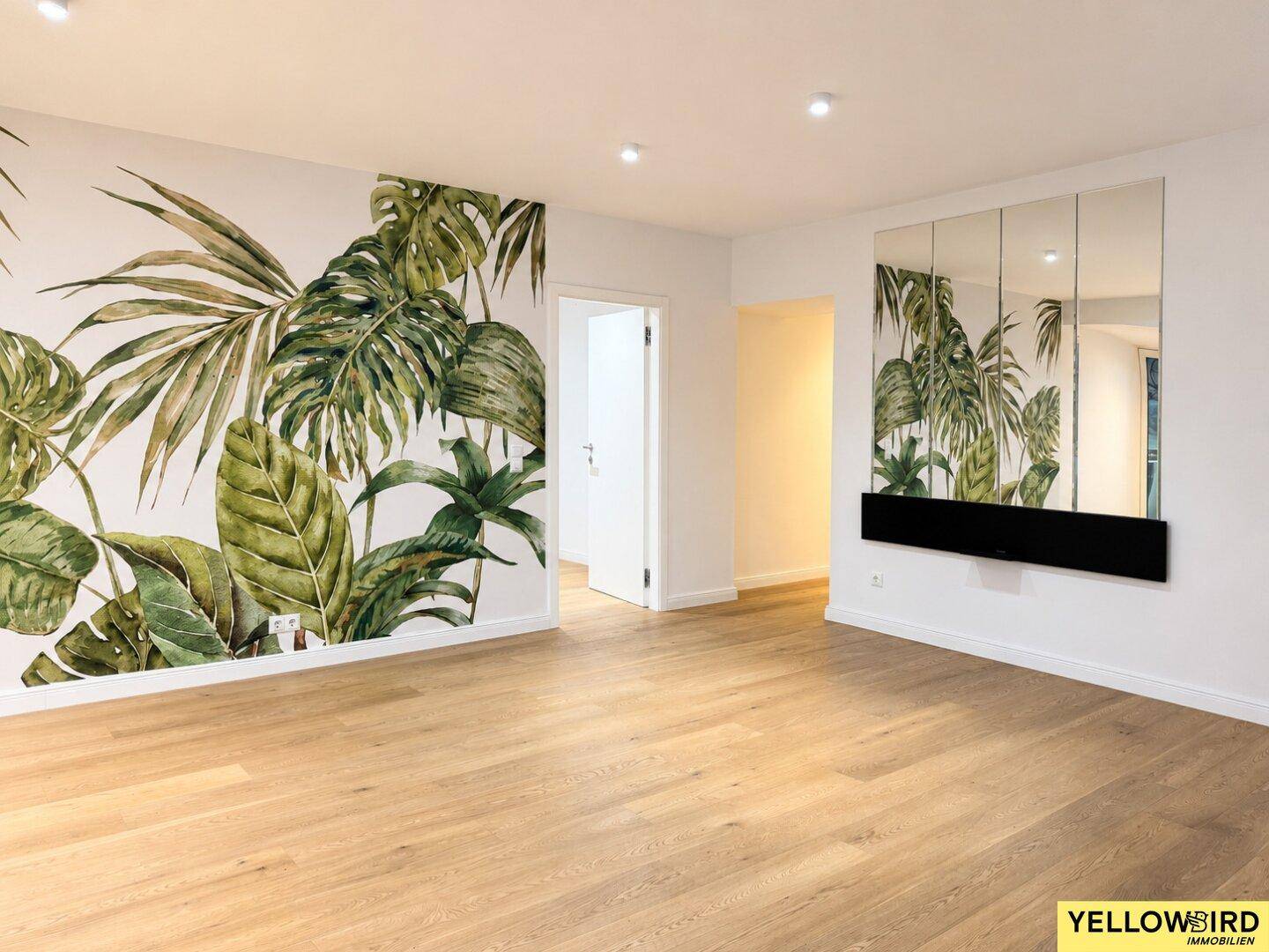 Geräumiges Wohnzimmer mit Holzboden, tropischer Wandtapete und einer dekorativen Spiegelwand.