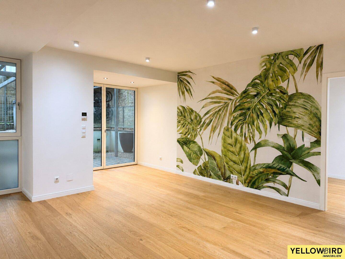 Helles Wohnzimmer mit Holzboden und auffälliger tropischer Tapete, die eine Wand schmückt.