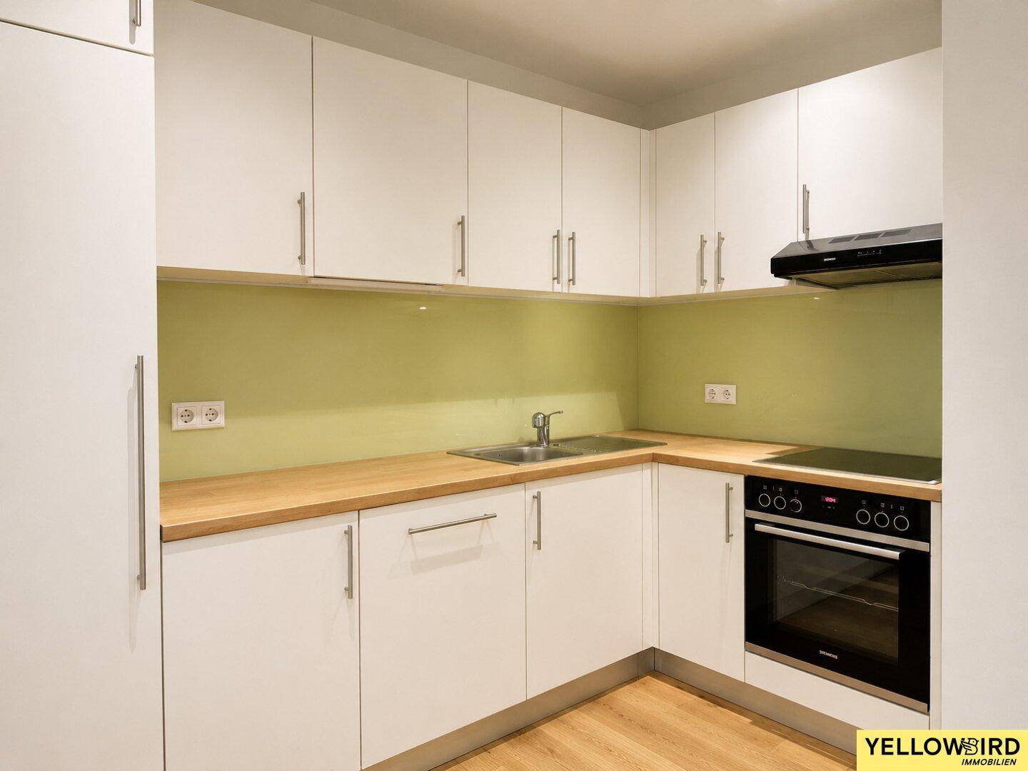 Moderne Einbauküche mit weißen Schränken, Holz-Arbeitsplatte und grünem Fliesenspiegel.