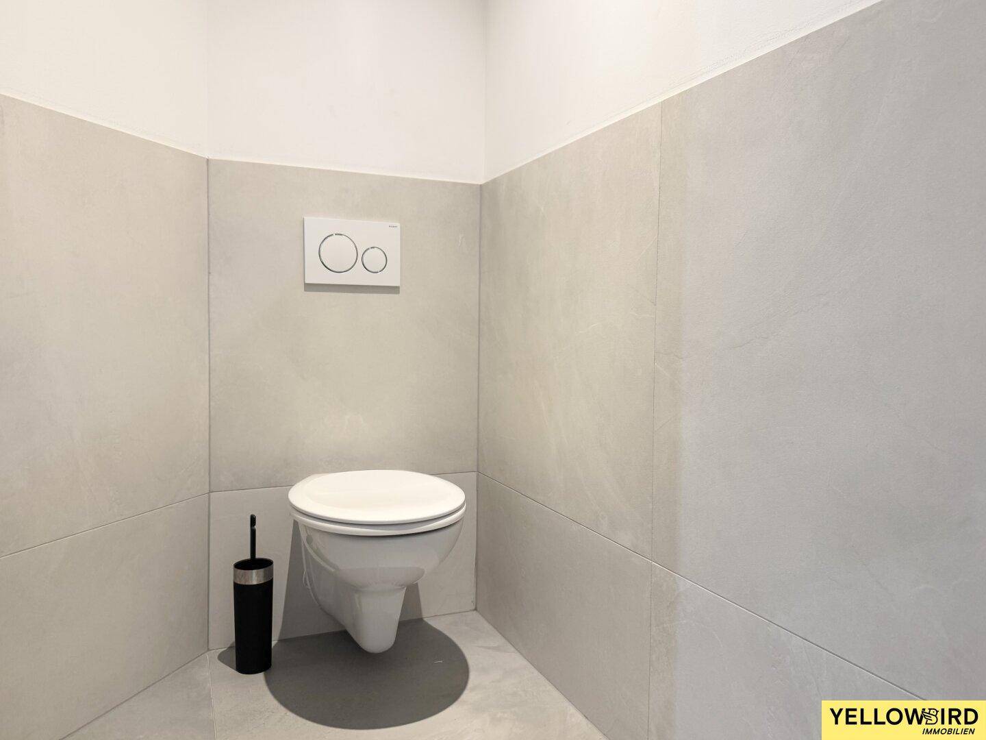 Separates WC mit wandhängender Toilette und hellen Fliesen an den Wänden.