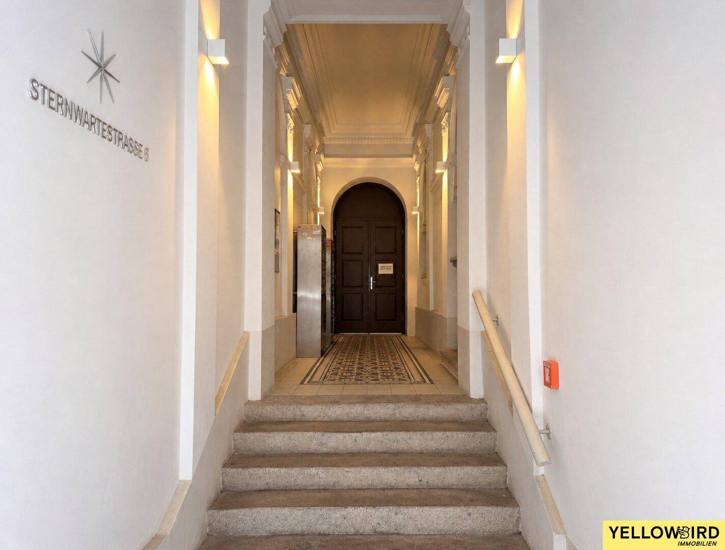 Historischer Eingangsbereich mit Treppe, hohen Decken und dekorativen Wandleuchten.