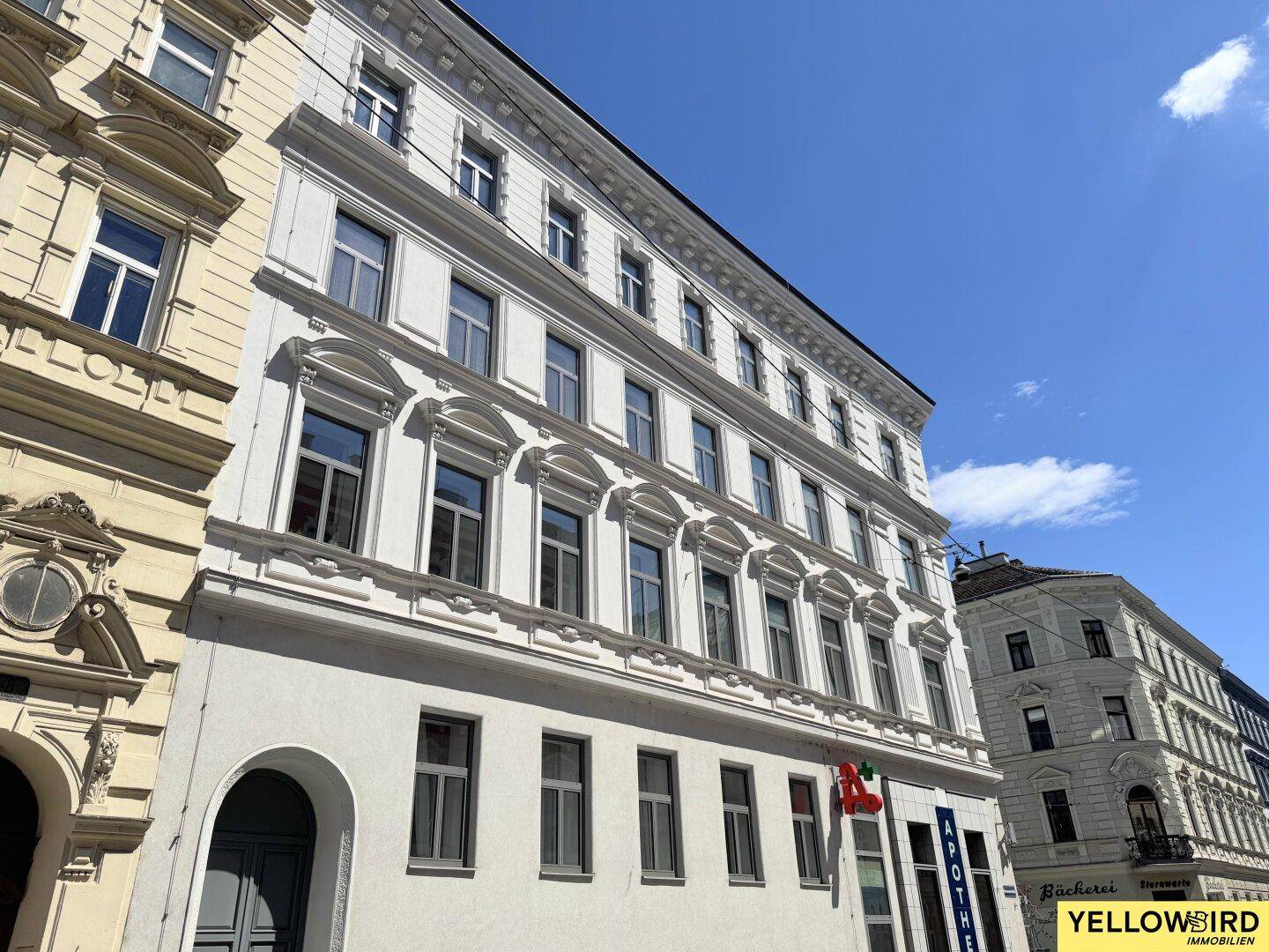 Historische Fassade eines Mehrfamilienhauses mit vielen Fenstern unter blauem Himmel.