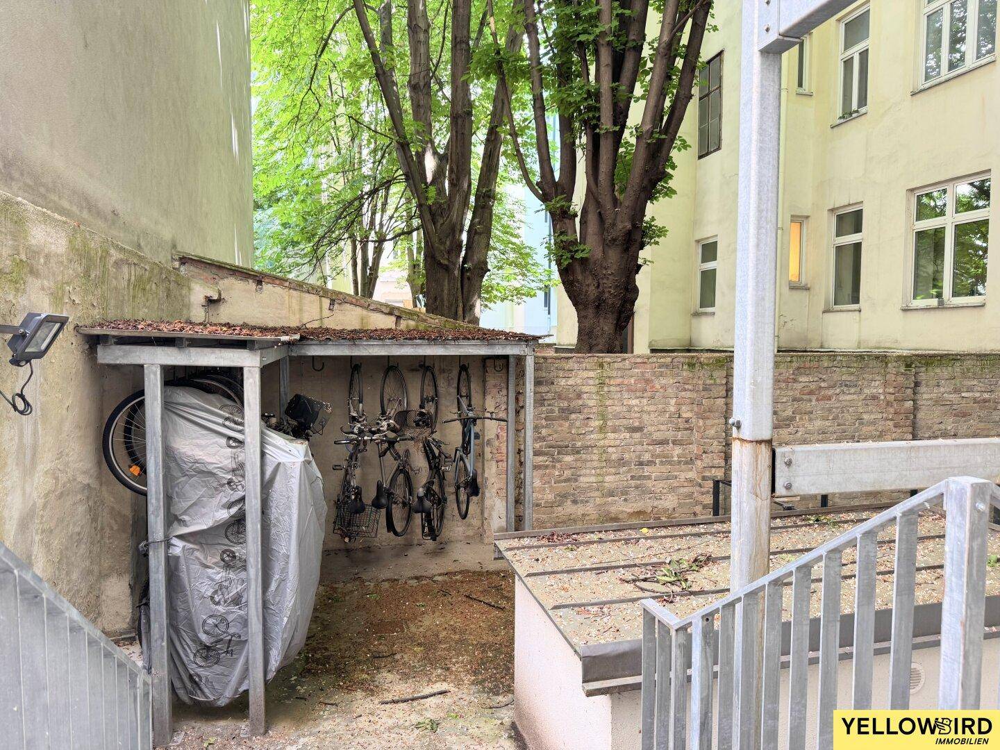 Überdachter Fahrradabstellplatz im Freien mit mehreren Fahrrädern und Backsteinmauer.