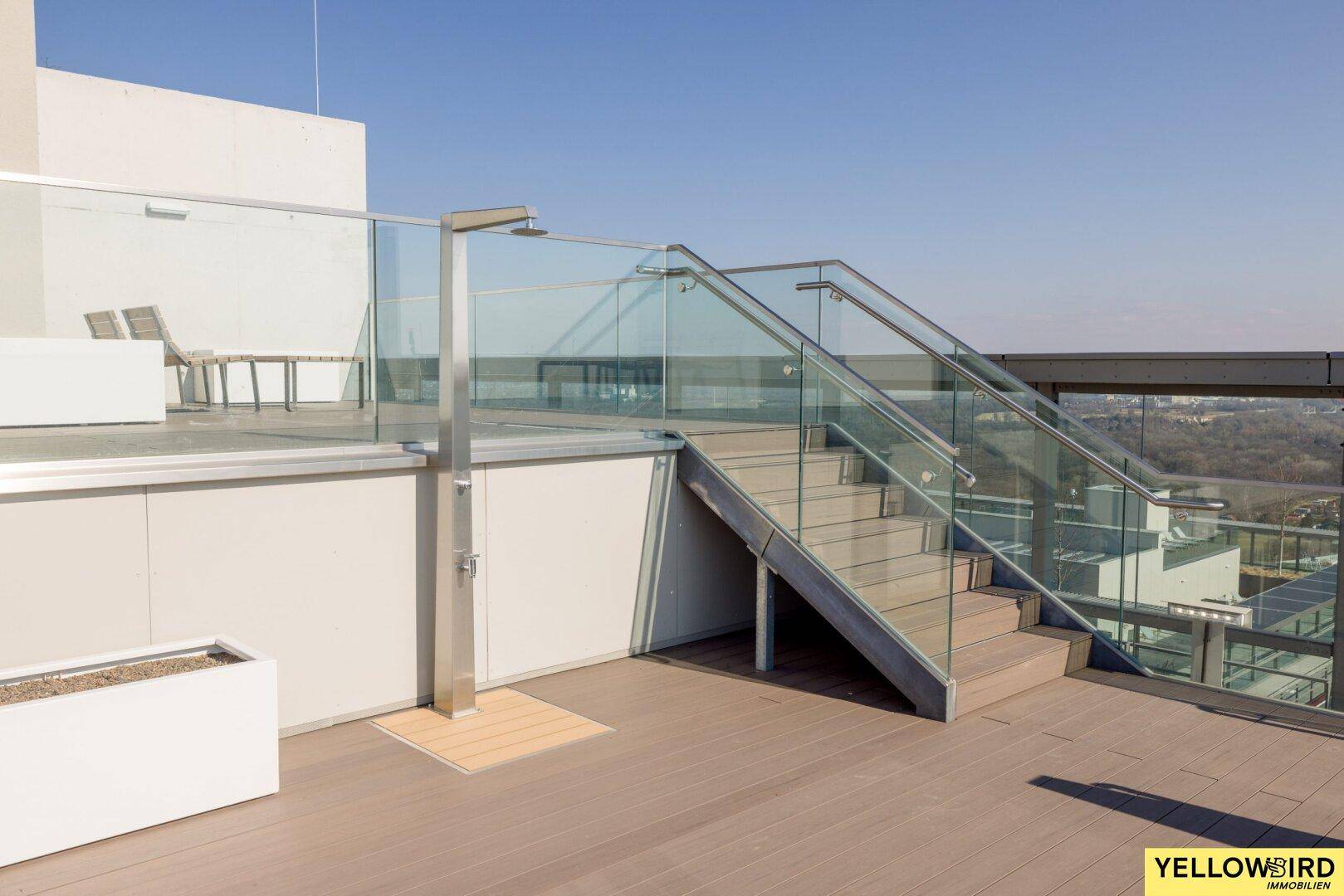 Zugang zur Dachterrasse mit Außendusche und Treppe, umgeben von modernen Glasgeländern.
