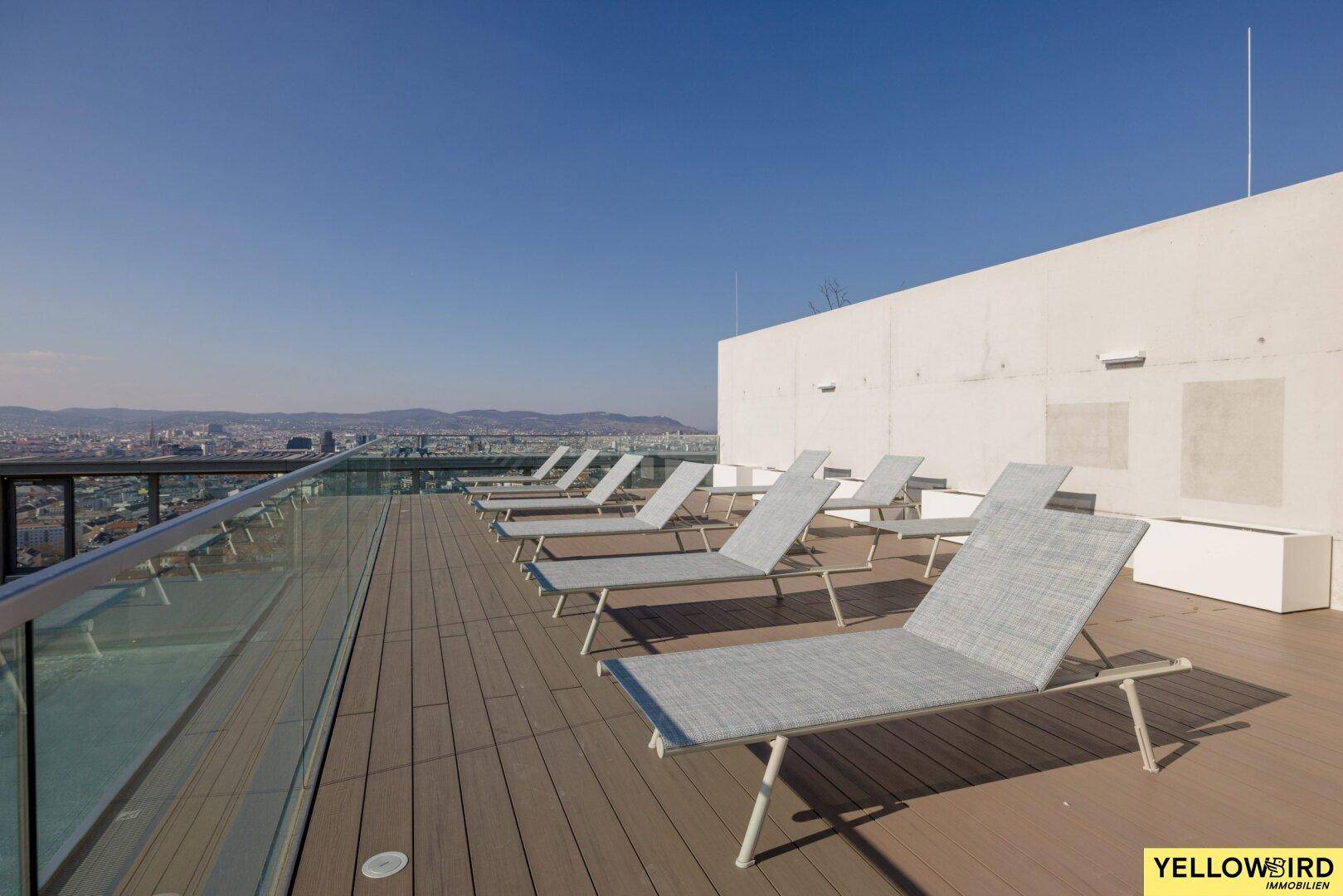 Sonnige Dachterrasse mit zahlreichen Liegestühlen und weitem Blick über die Stadtlandschaft.