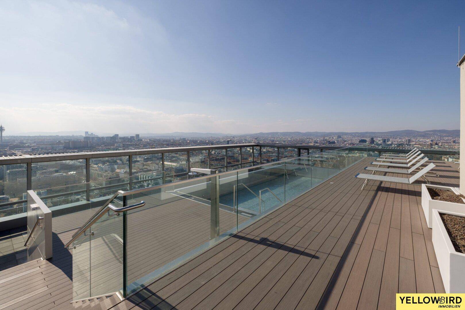 Weitläufige Dachterrasse mit Pool, Liegestühlen und Panoramablick über die Stadtkulisse.