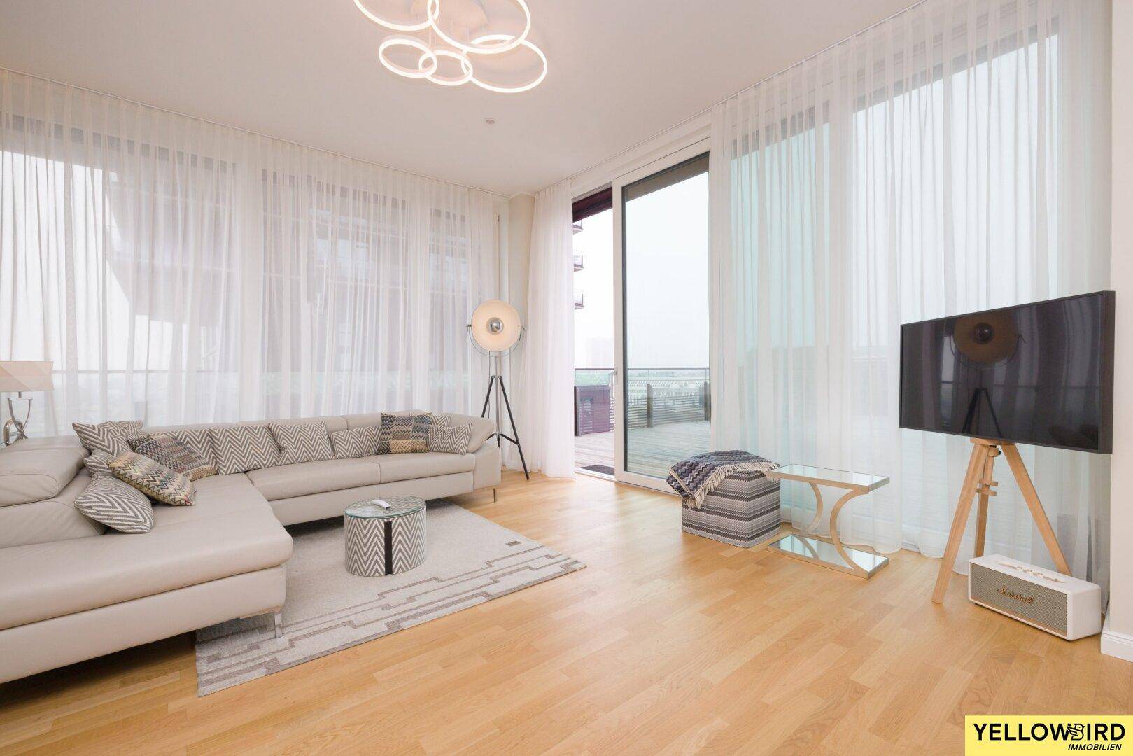 Lichtdurchflutetes Wohnzimmer mit großzügigen Fenstern, hellem Sofa und Holzboden.