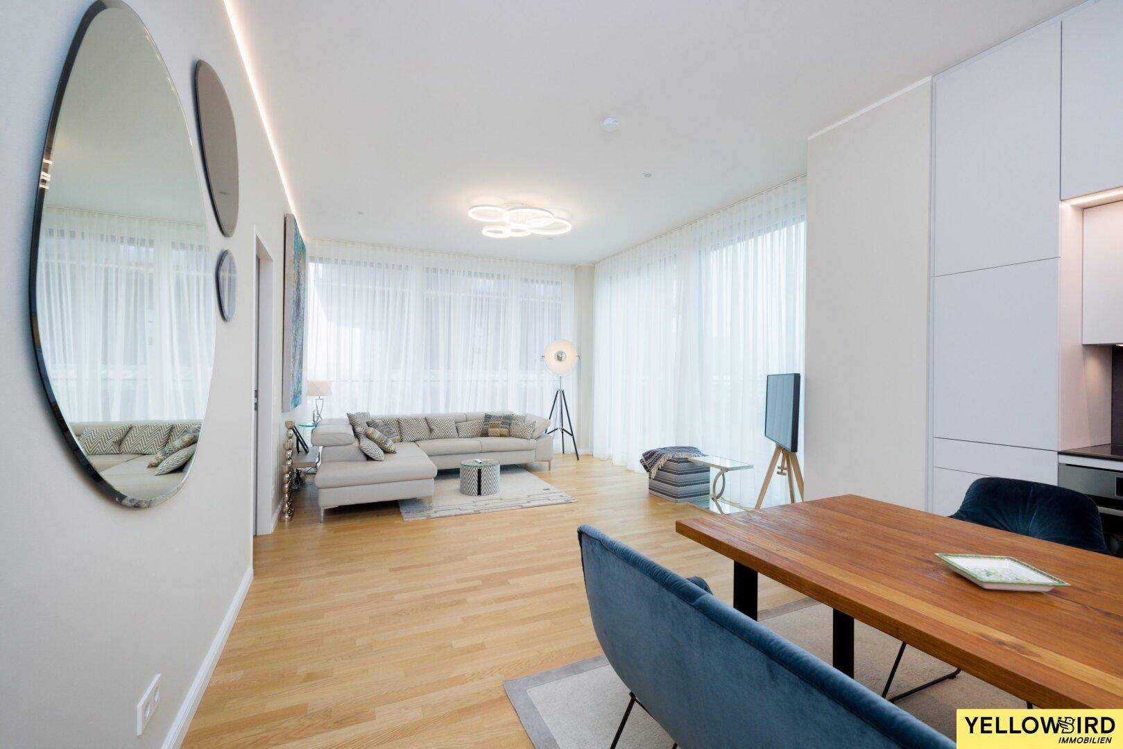 Geräumiger Wohn-Essbereich mit großen Fenstern, hellem Sofa und Holzboden.