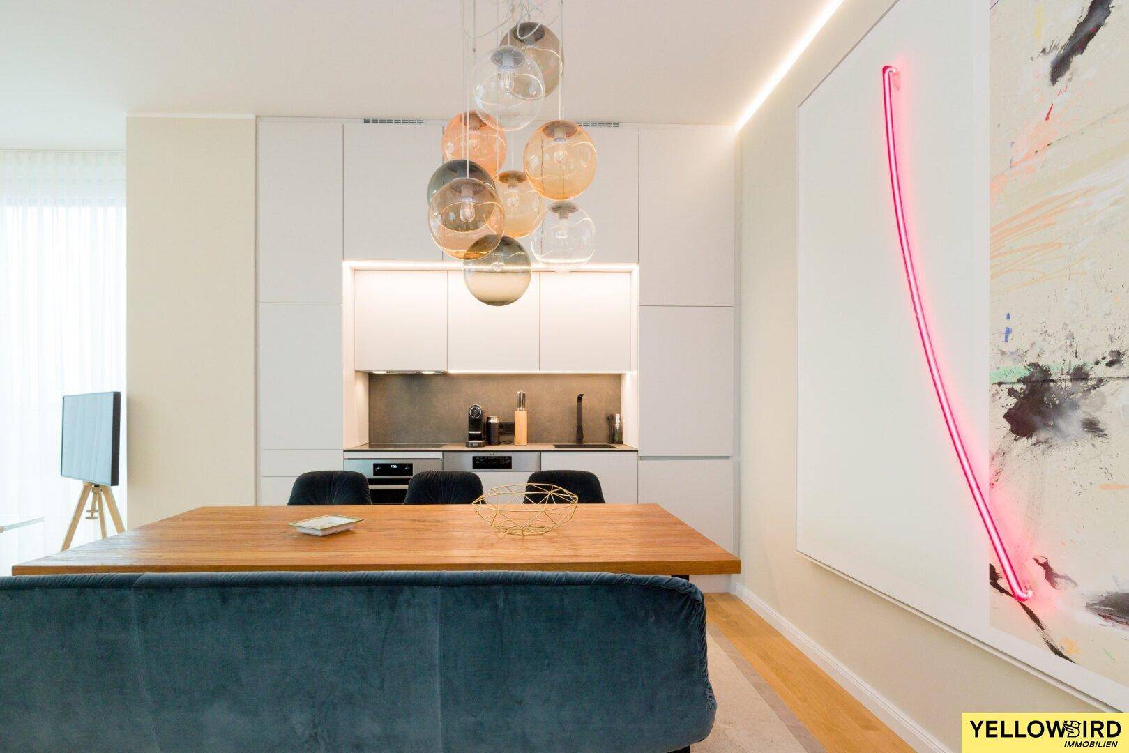Integrierte, moderne Küche mit weißen Schränken, Holztisch und Designer-Pendelleuchte.