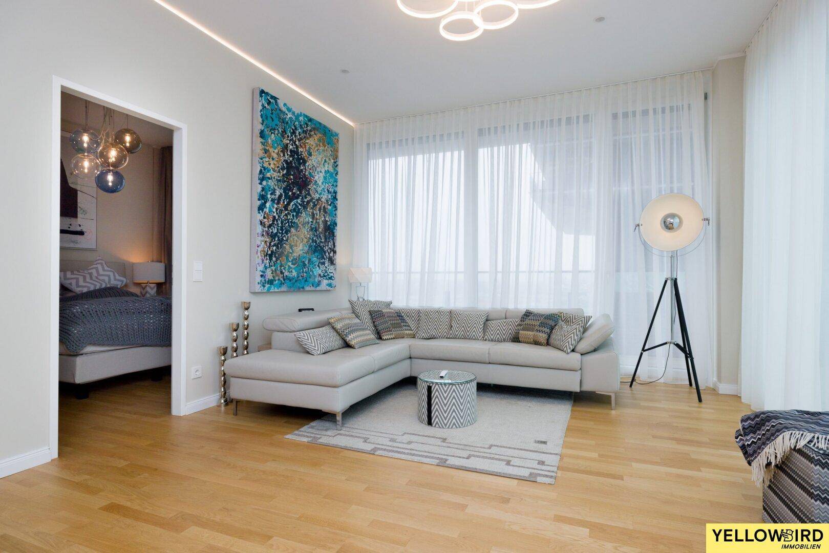 Helles Wohnzimmer mit großem Ecksofa, Kunstwerk und Zugang zum Balkon.