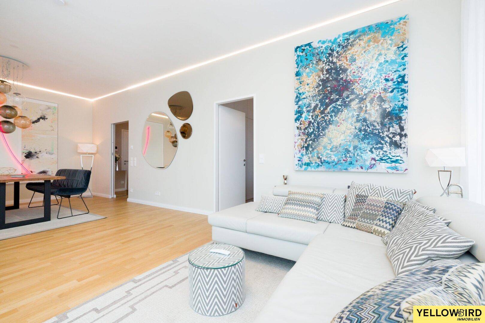 Heller, offener Wohn-Essbereich mit modernem Sofa, Kunstwerken und Holzboden.
