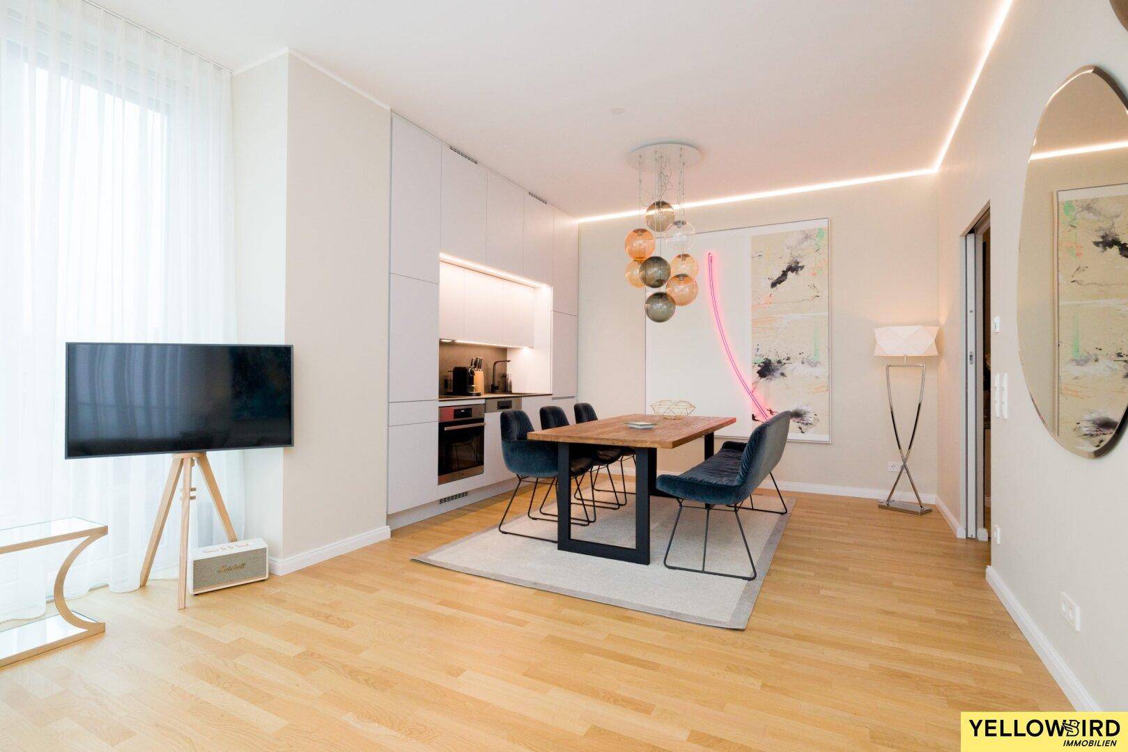 Moderner Wohn-Essbereich mit integrierter Küche, Holztisch und Fernseher auf Ständer.