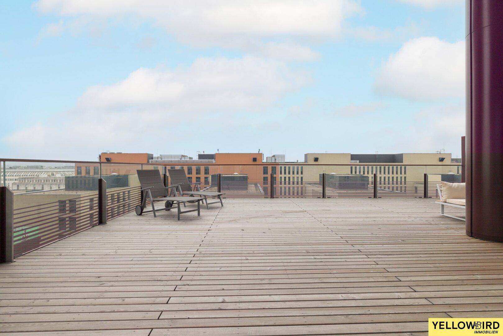 Weitläufige Holzterrasse mit Liegestühlen und Blick auf die umliegenden Gebäude.