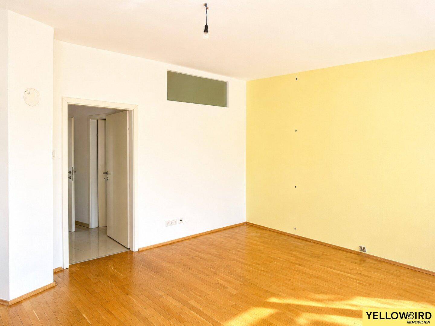 Geräumiger Wohnraum mit Holzboden und einer auffälligen gelben Akzentwand.