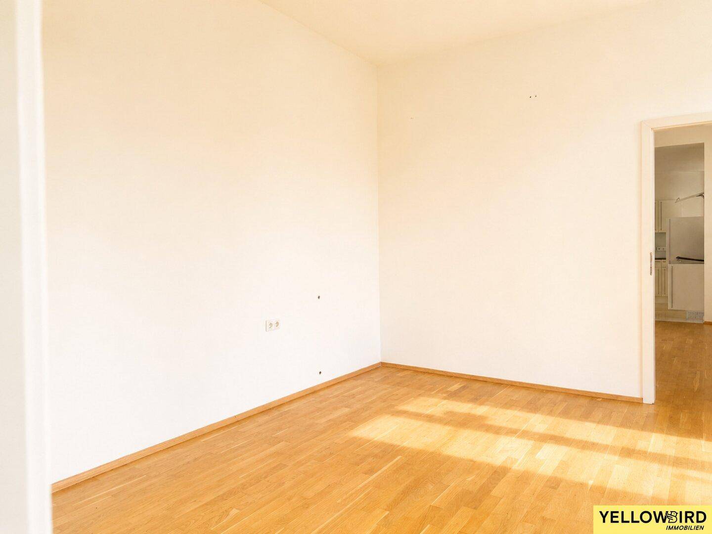 Heller, leerer Raum mit Holzboden und Zugang zu einem weiteren Zimmer.
