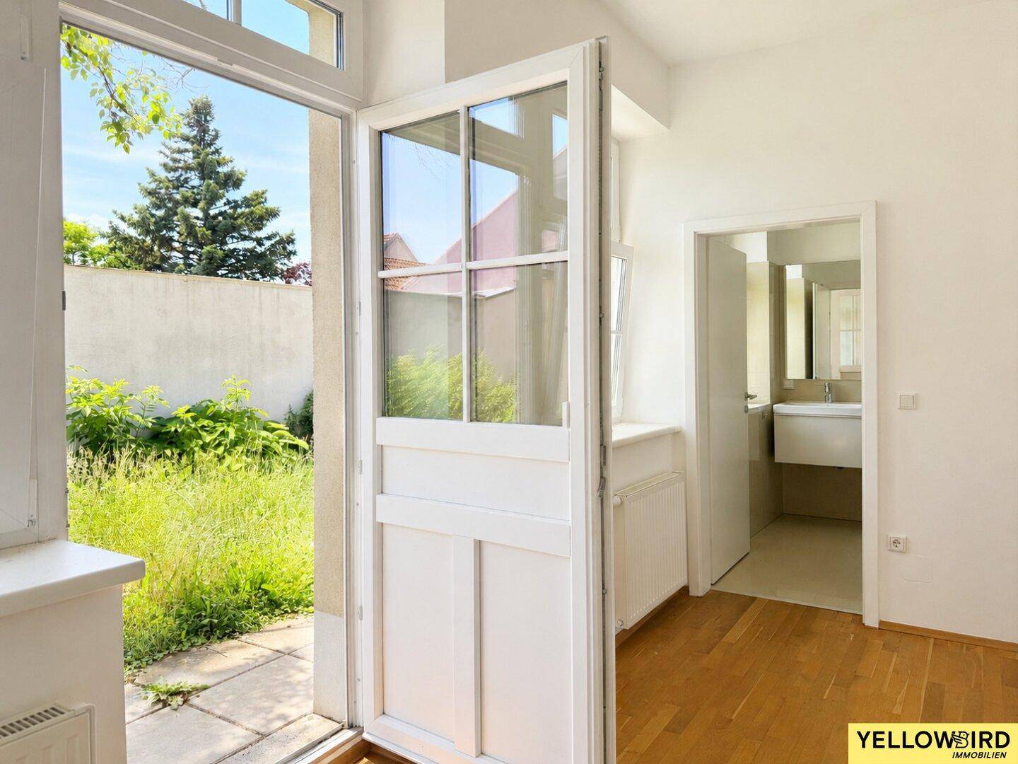 Heller Eingangsbereich mit Holzboden und Zugang zu einem verwilderten Garten.