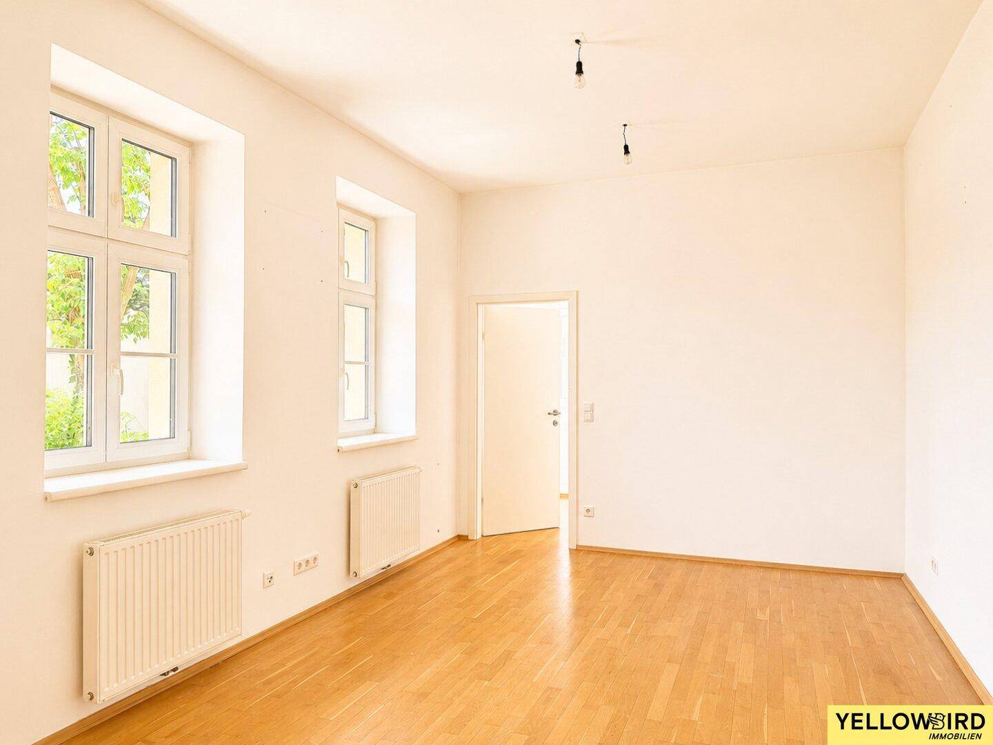 Leerer Raum mit Holzboden und zwei Fenstern, bereit zur individuellen Gestaltung.