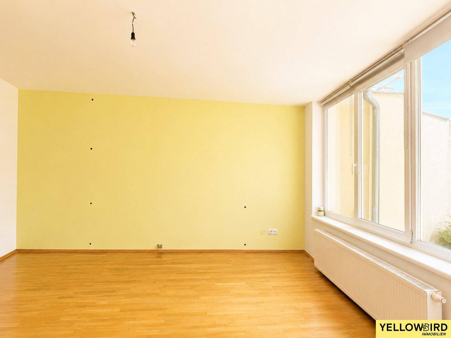 Lichtdurchfluteter Raum mit großen Fenstern und Holzboden, ideal für ein Wohnzimmer.