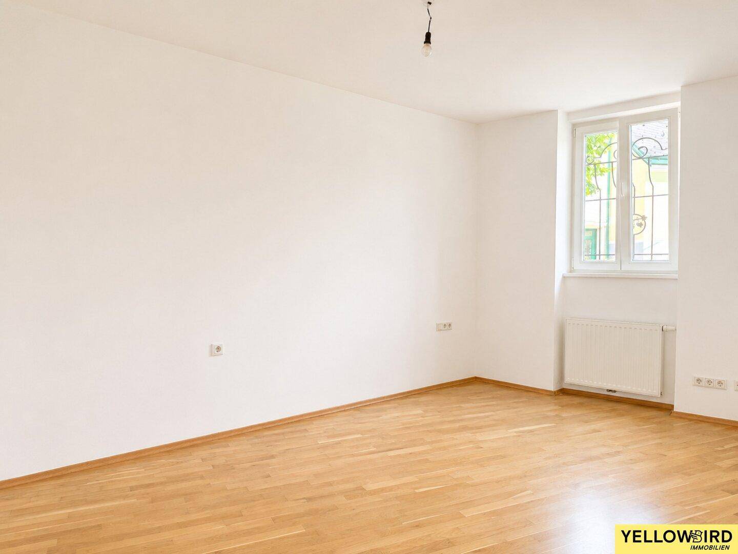 Helles Schlafzimmer mit Holzboden und einem Fenster, das viel Tageslicht hereinlässt.