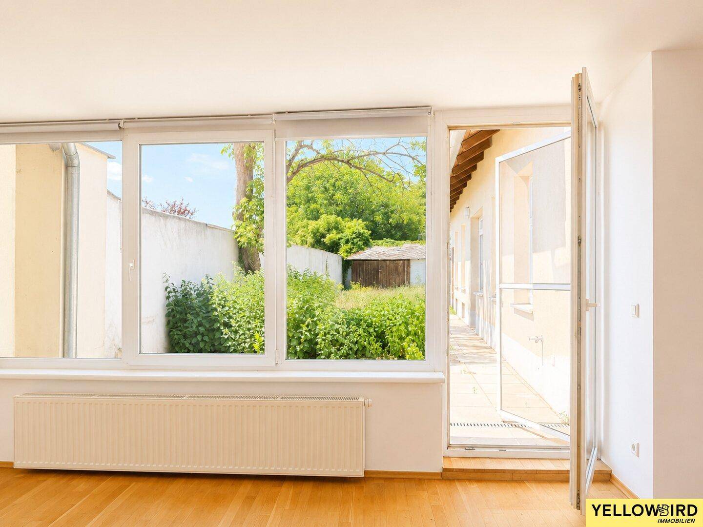 Lichtdurchfluteter Wohnraum mit großen Fenstern und Ausblick auf den grünen Gartenbereich.
