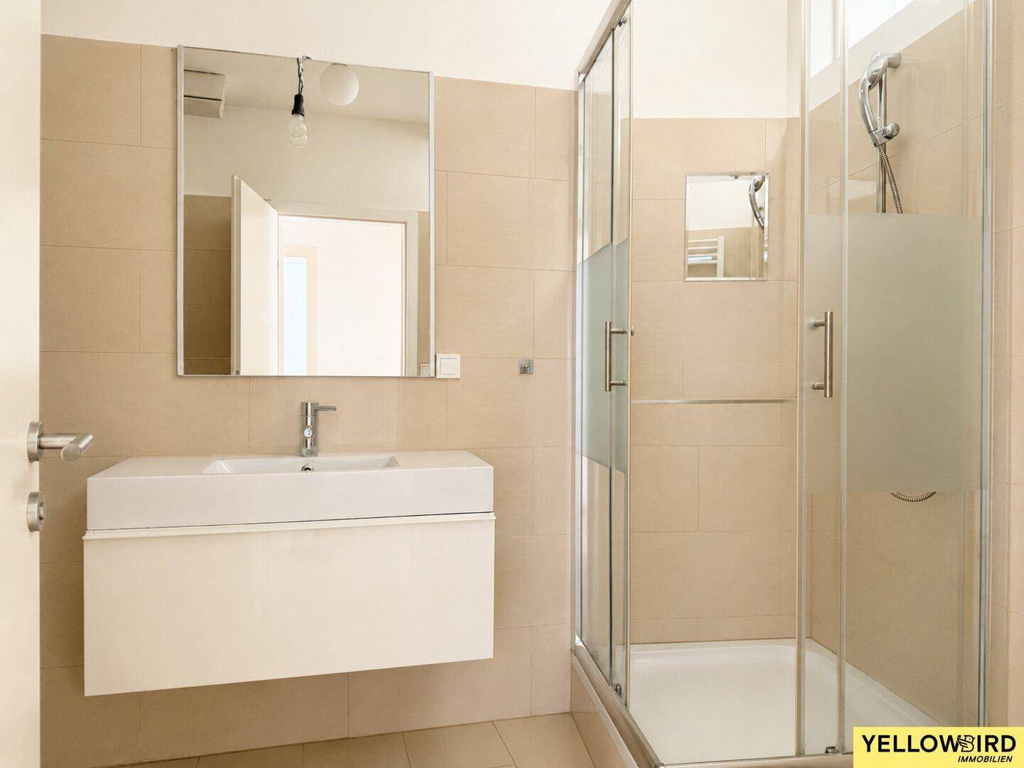 Helles Badezimmer mit modernem Waschbecken, Duschkabine und großem Spiegel.
