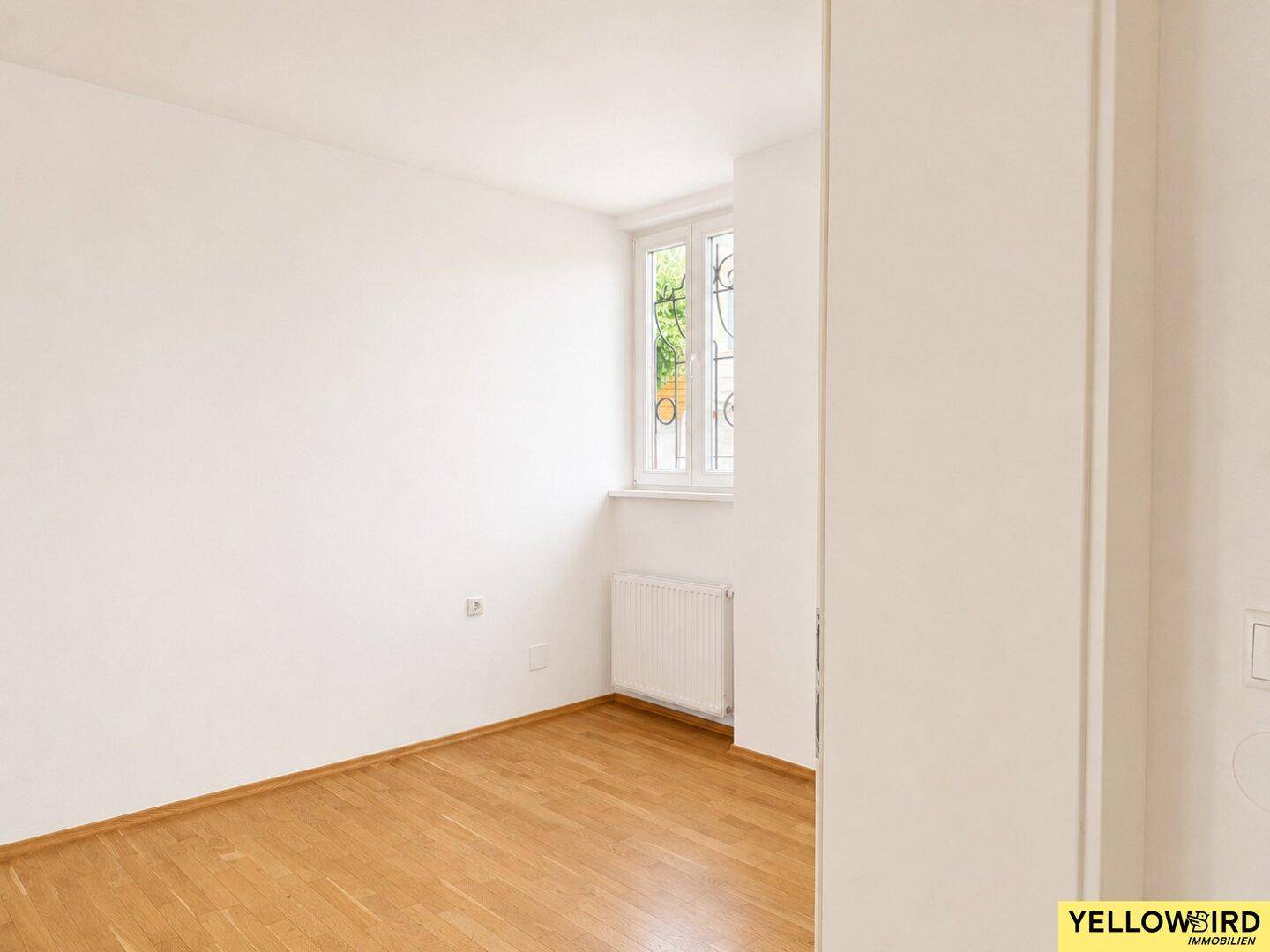 Leeres Schlafzimmer mit Holzboden und einem Fenster, ideal für ein Kinder- oder Gästezimmer.