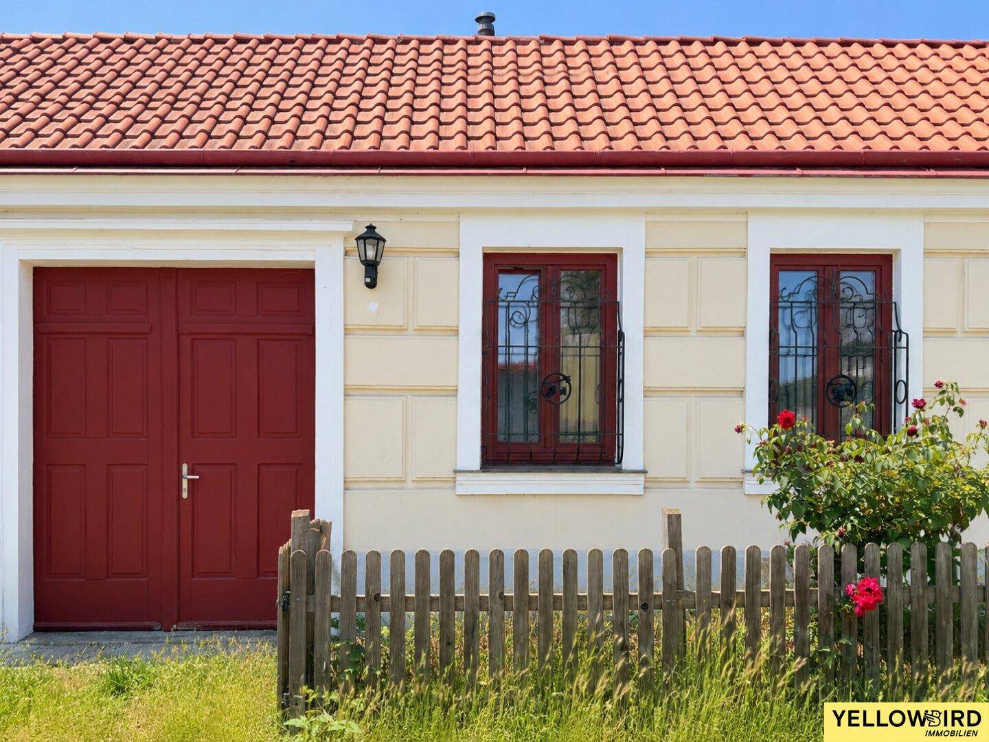 Detailansicht der Hausfassade mit roter Doppeltür, Fenstern und einem Holzzaun.