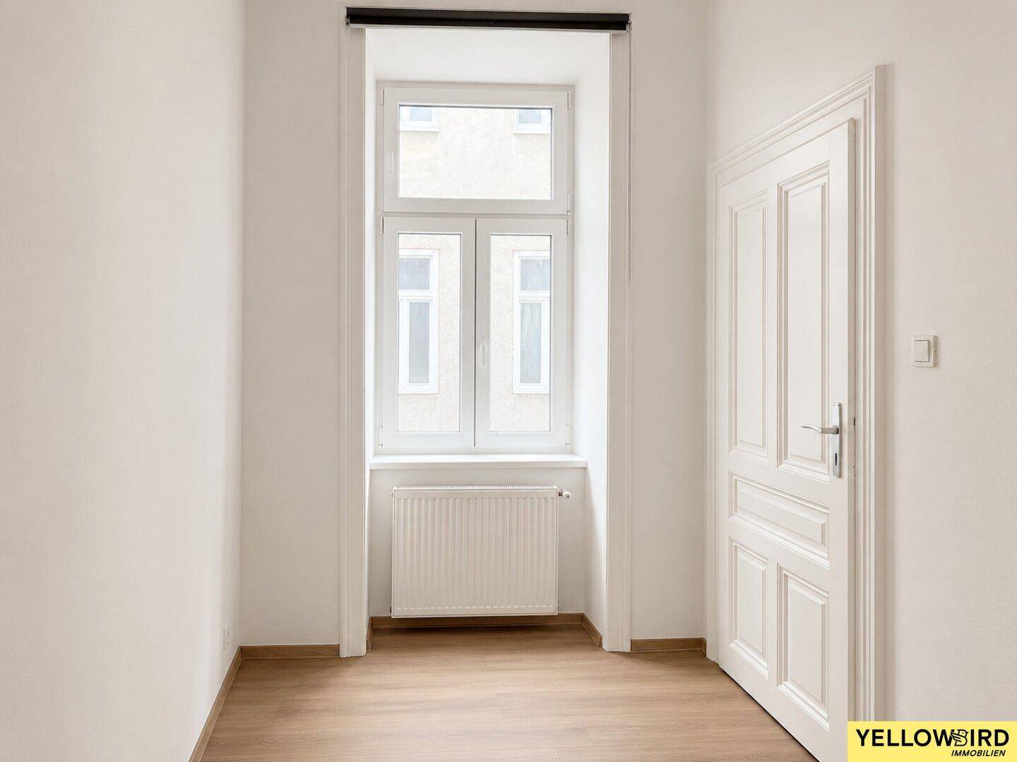 Schmaler Raum mit Fenster, Heizkörper und weißer Holztür.