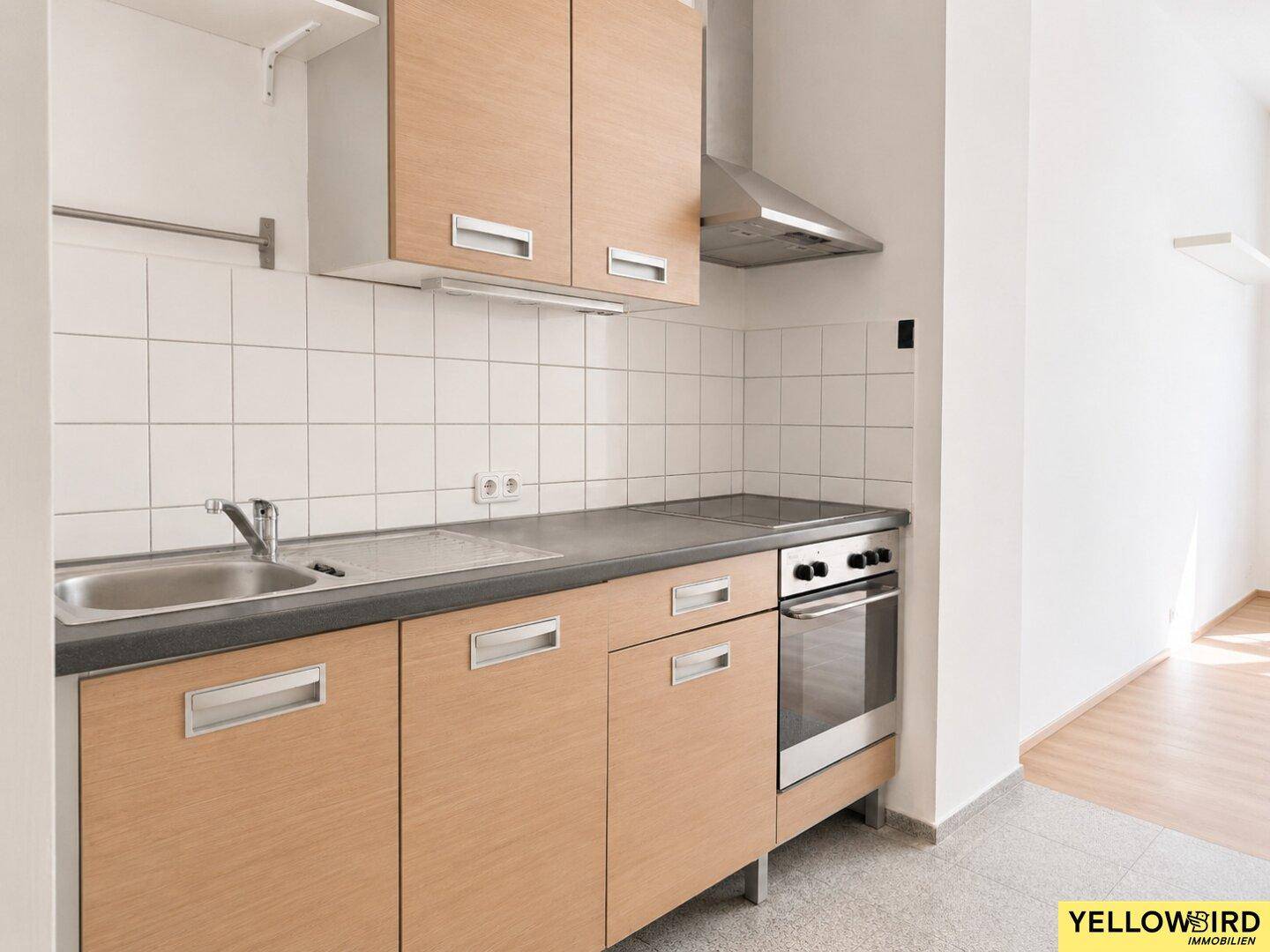 Funktionale Einbauküche mit Holzfronten, Spüle, Herd und Dunstabzugshaube.