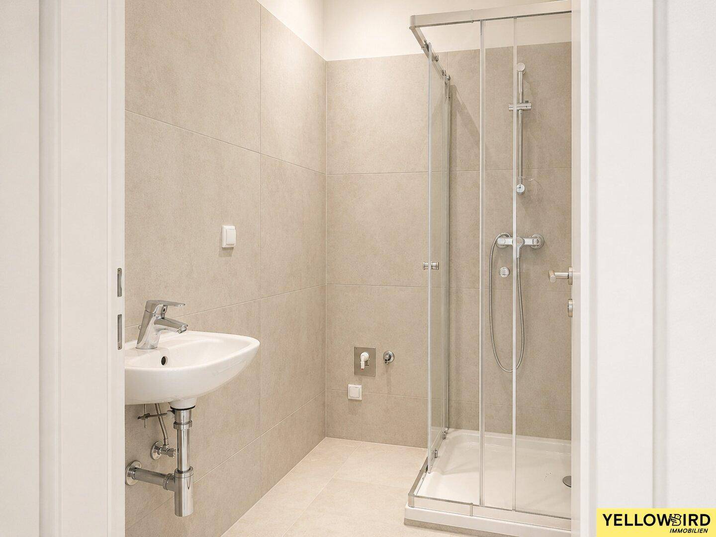 Modernes Badezimmer mit Duschkabine, Waschbecken und hellen Fliesen.